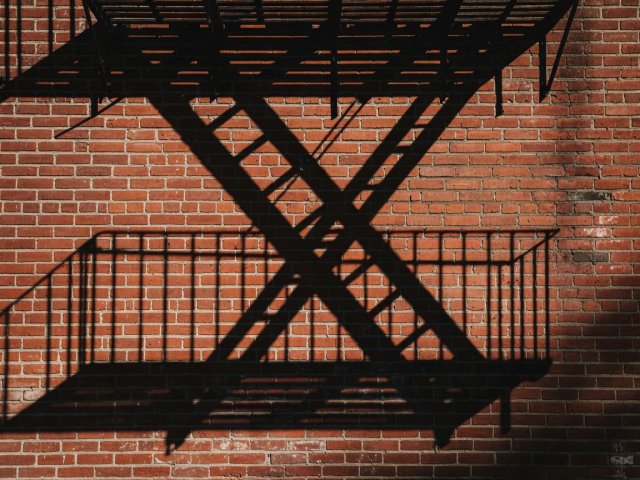 Crisp zigzag shadow of an iron fire escape projected onto weathered red brick wall at late afternoon