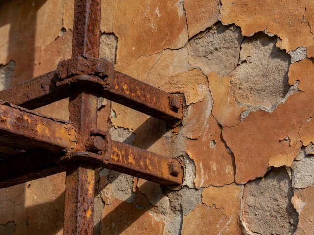 Close-up texture of rusted iron scaffolding clamps against a peeling ochre and terracotta plaster facade